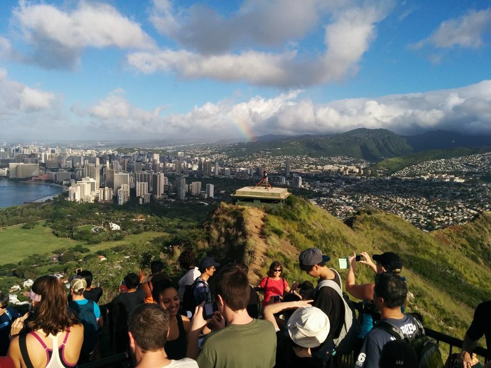 Image of tourists on top of Diamond Head near Honolulu, with the city and a rainbow in the background.