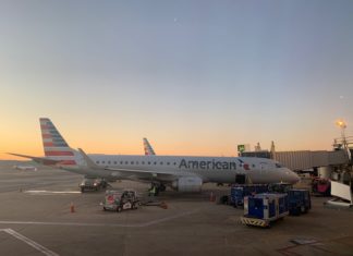 An American Airlines plane sits at the gate with a sunset in the background