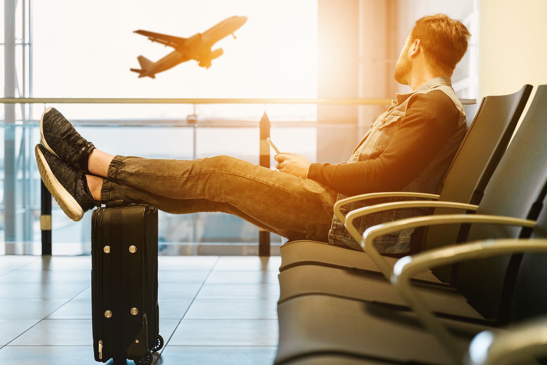 Image of man with foot on top of suitcase, waiting at airport - a perk of United Silver status is that he can check a bag for free, providing extra value on each flight