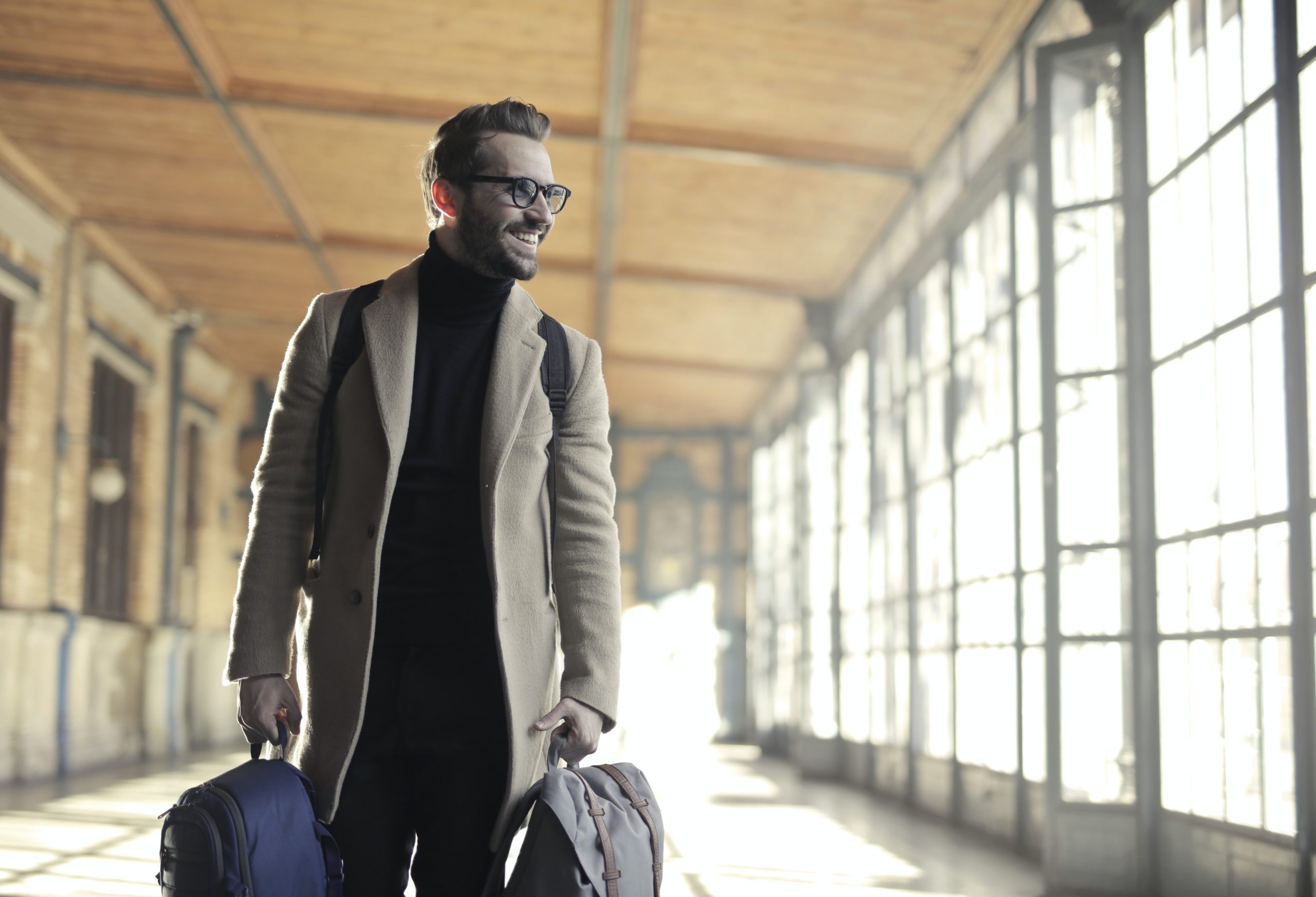 A man carries 2 small suitcases through an empty airport hallway