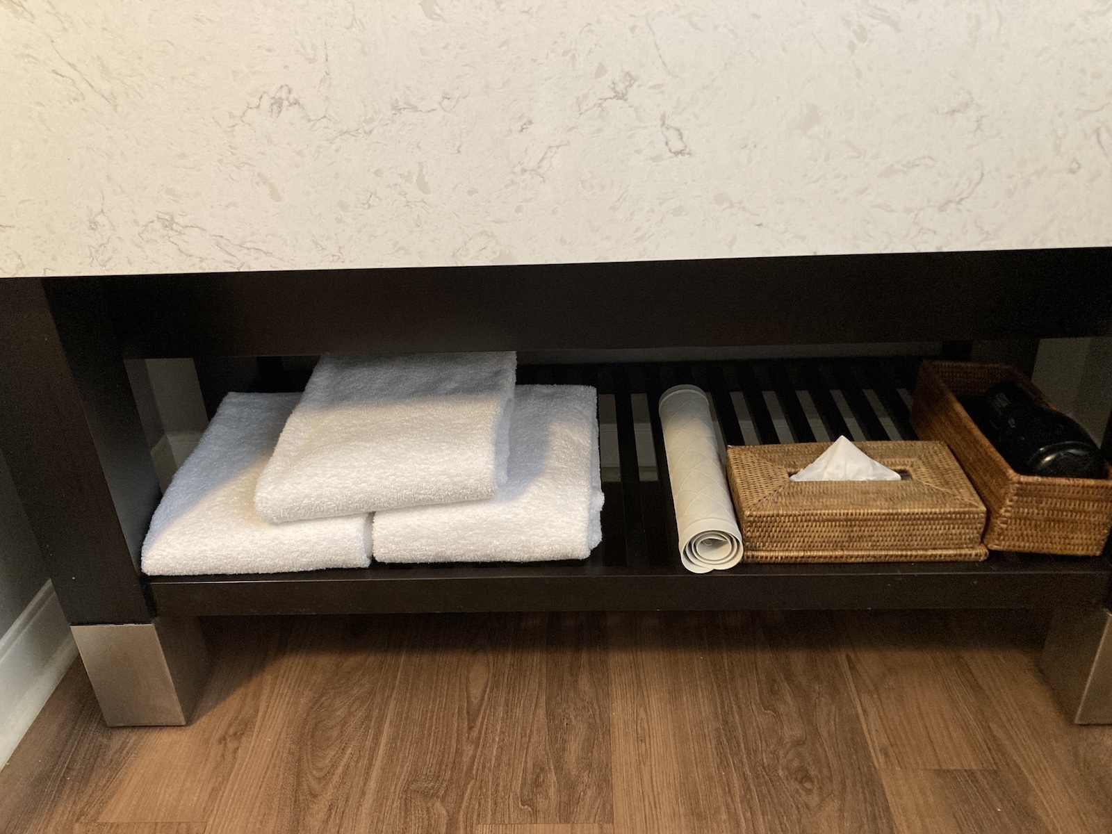 Image shows towels, rug, and hair dryer located on a shelf under a sink