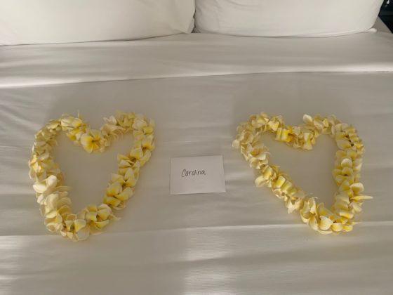 Photo of 2 leis in heart shapes with a note between them, on top of a bed