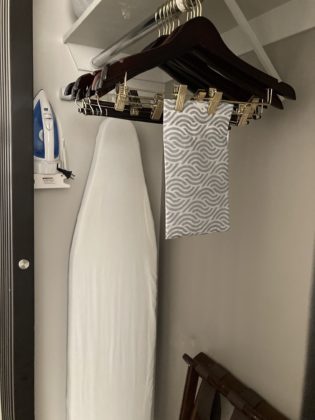 An empty closet has empty hangers with an iron and ironing board beyond