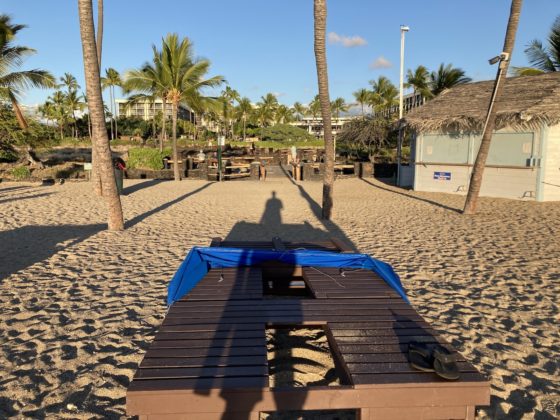 Photo of a person's shadow falling onto a lounge chair on a beach