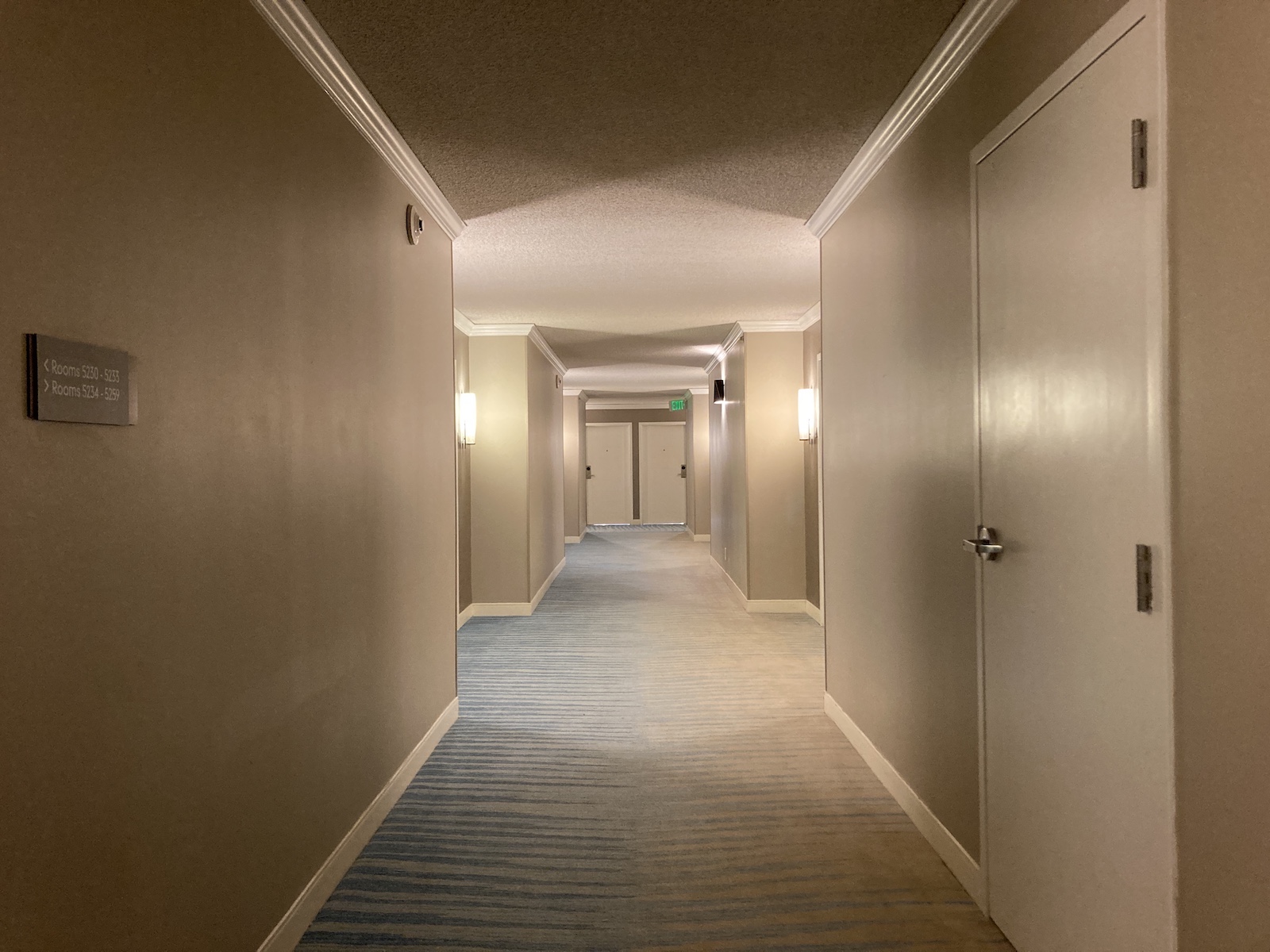 Photo of an empty hallway well lit at a hotel, with doors along the corridor