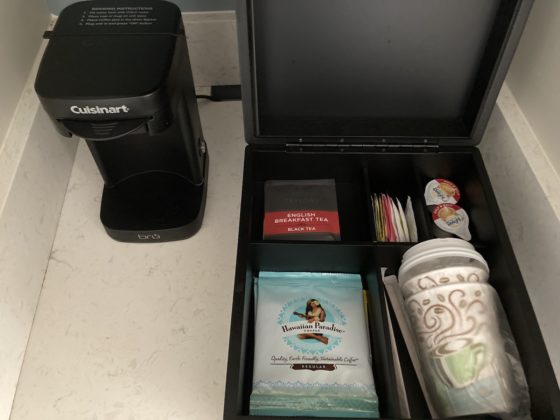 A small single-serve coffee machine sits next to a box with coffee and tea supplies