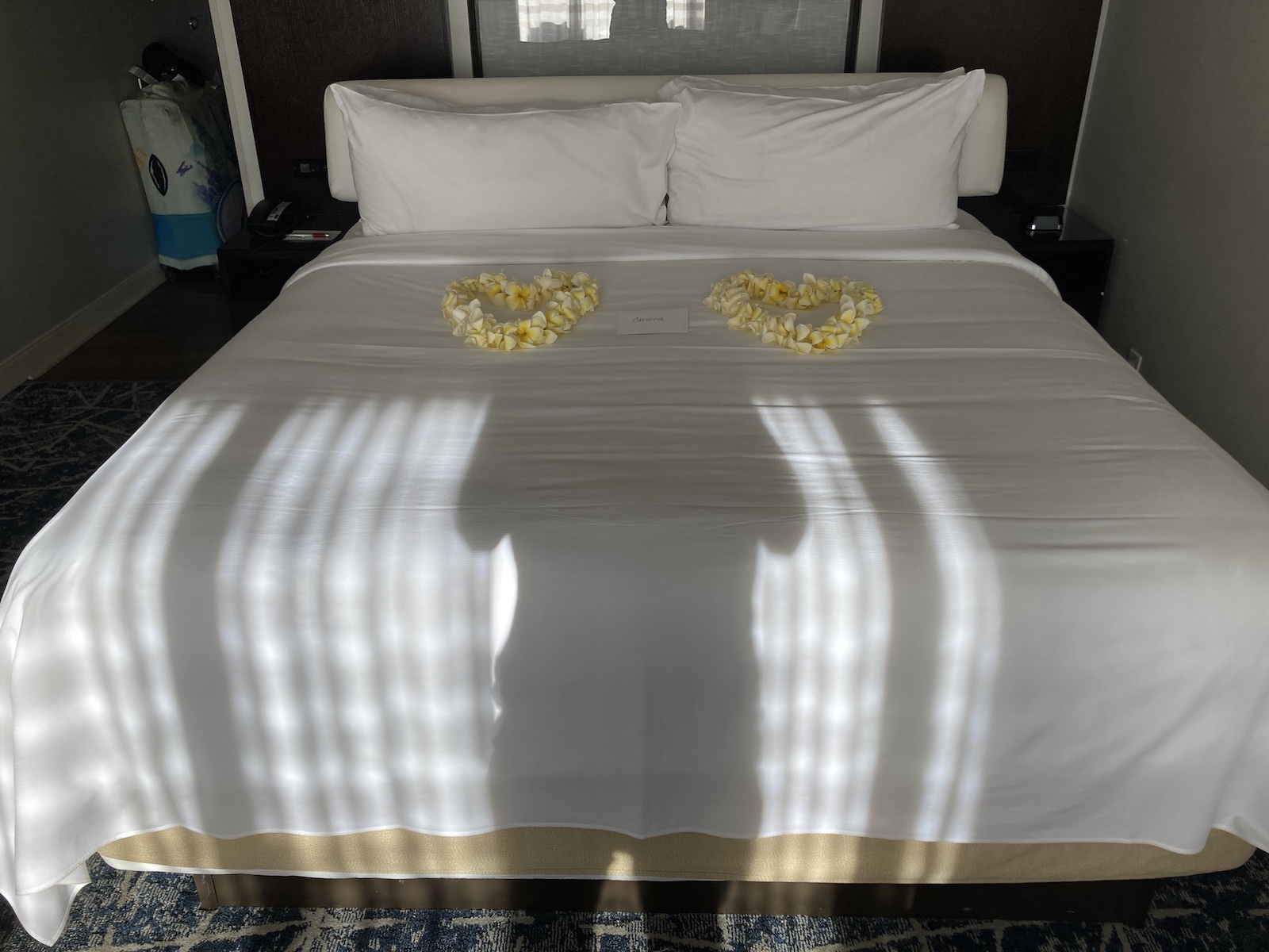 Photo of a bed with white sheets and pillows on it, plus two flower leis in the shape of hearts