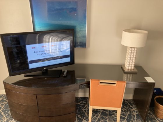 a large wooden desk-dresser combination has a TV and lamp on top plus a chair