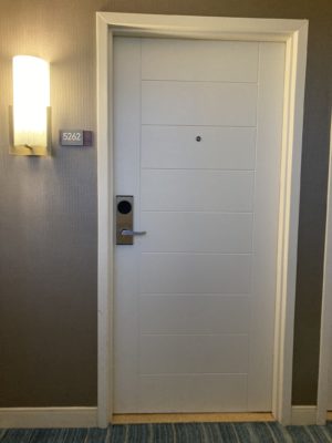 A lamp sits on the wall next to the sign "5262" and the white door to enter the hotel room