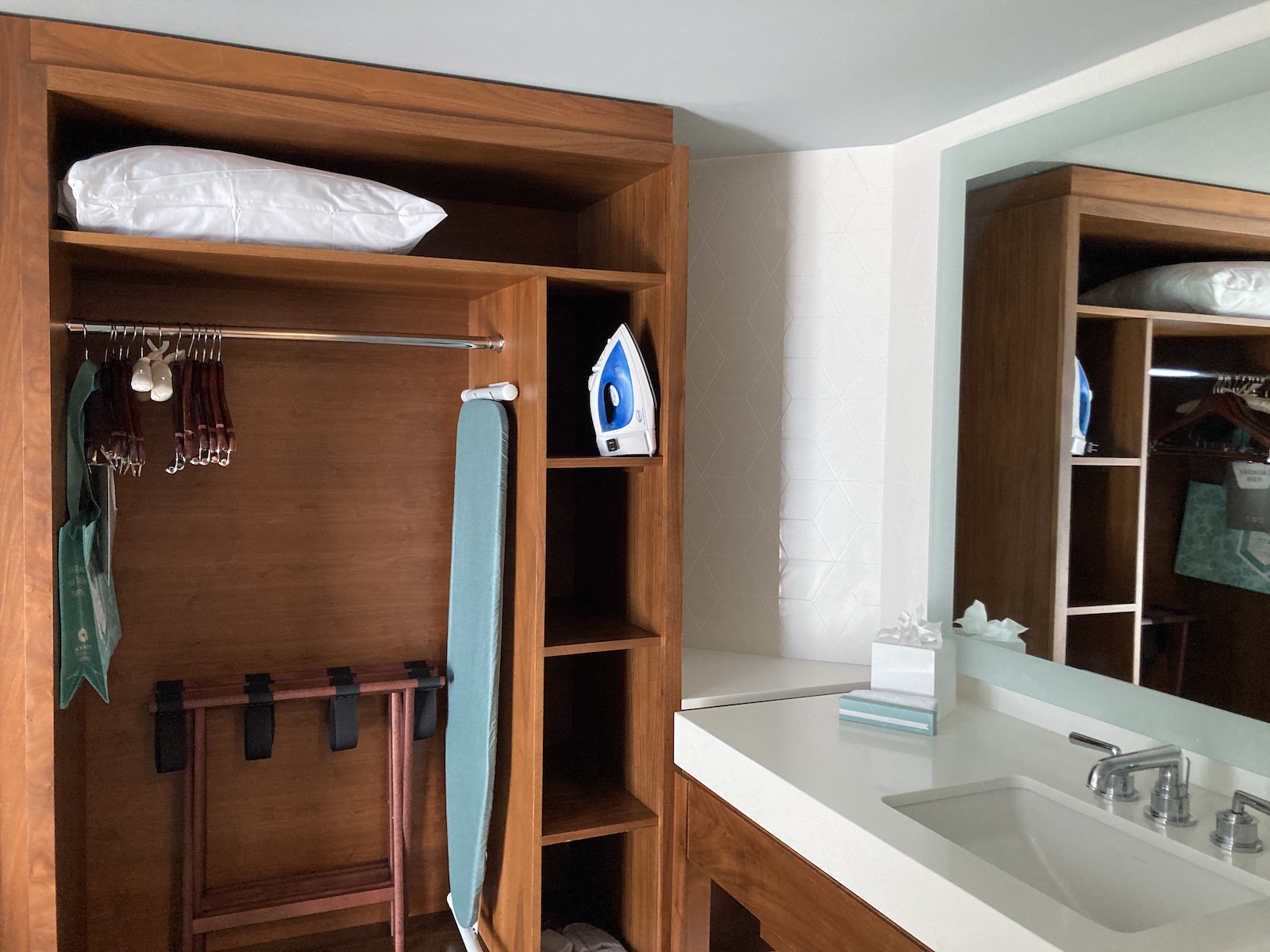 Photo shows an open closet next to a sink, with iron, ironing board, luggage rack, and spare pillow inside the closet in our suite at Hyatt Regency Waikiki