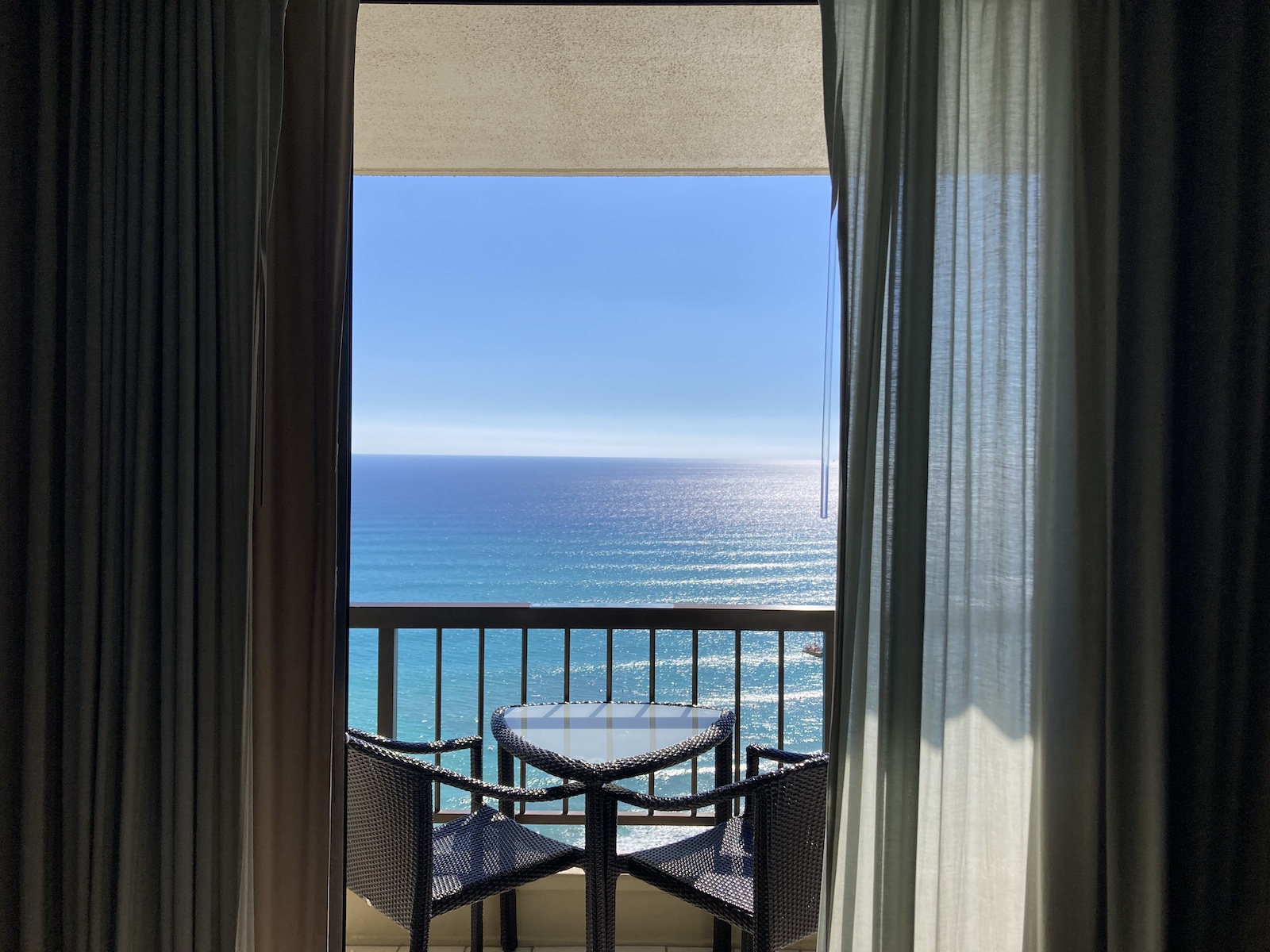 Photo of the glass sliding doors opening to a balcony with 2 chairs and small table, looking over the ocean and beach from our room at Hyatt Regency Waikiki