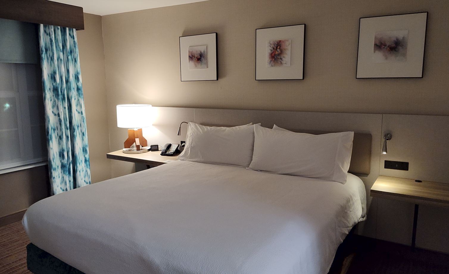 a bed with white sheets and a lamp on a desk